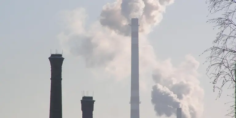 Tall industrial chimneys releasing smoke into a pale sky