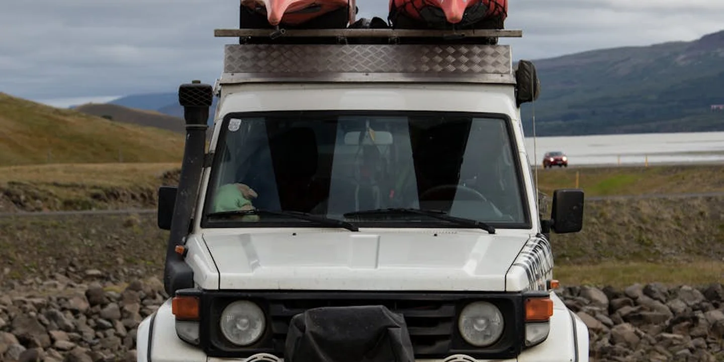Front view of a white SUV with two kayaks secured on a roof rack, against a coastal landscape with hills in the background.