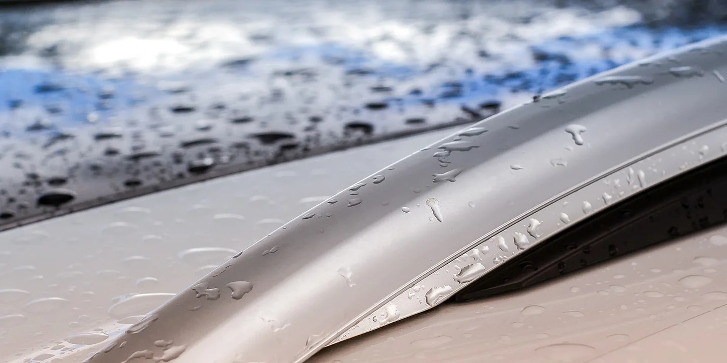 Close-up of a kayak secured to a roof rack with water droplets on its surface, illustrating wet conditions during rain.