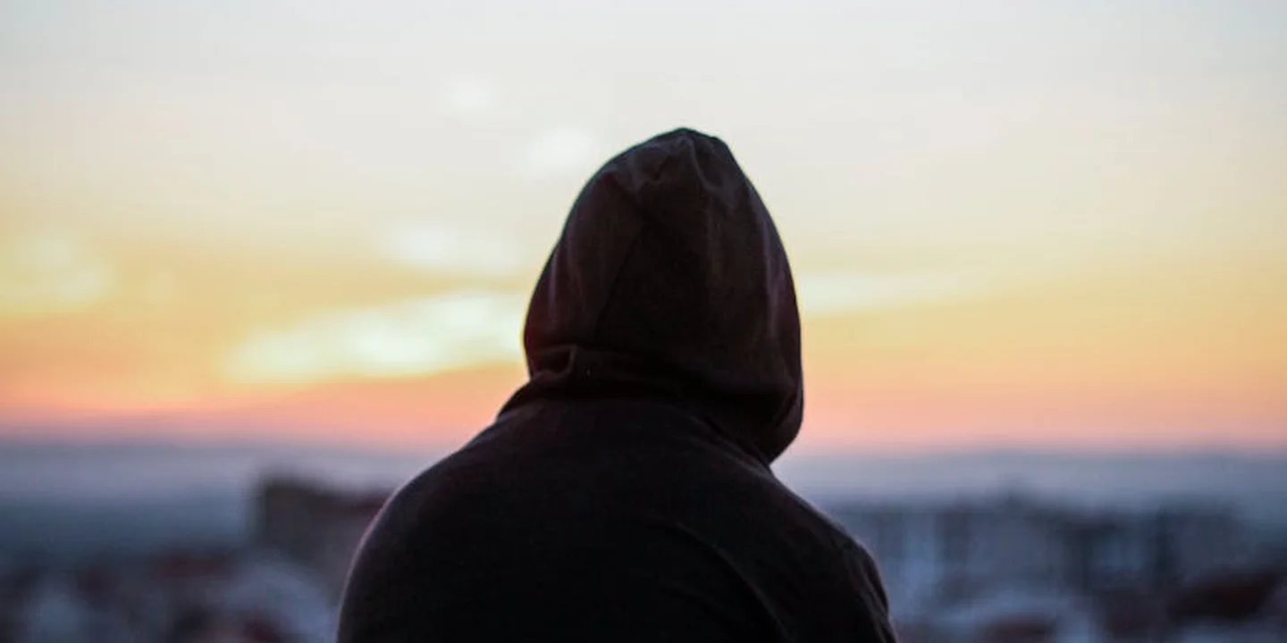 Silhouetted figure wearing a hooded jacket, facing away at a sunset, symbolizing the hidden health risks of lead exposure in roofing work.