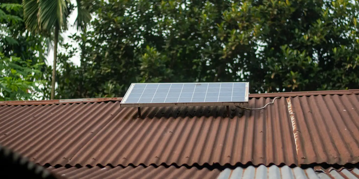 Brown corrugated metal roof with a small solar panel mounted on top, with trees in the background.