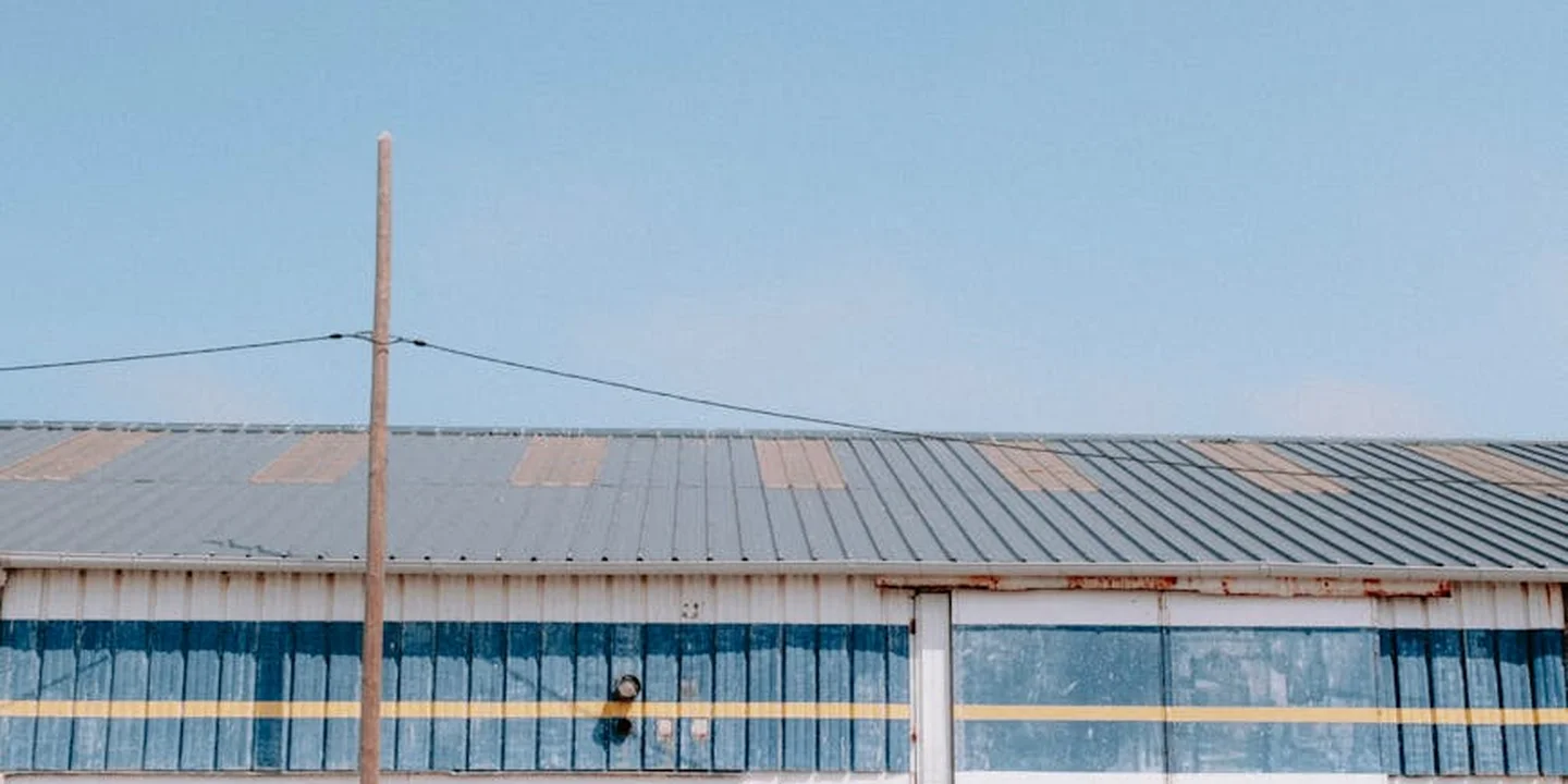 Wide shot of a metal roof with a blue-gray hue, a wooden utility pole and wires in the foreground, under a clear blue sky.