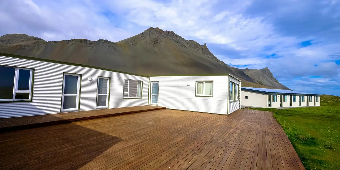 Row of white modular homes with a long wooden deck and a mountain range in the background.