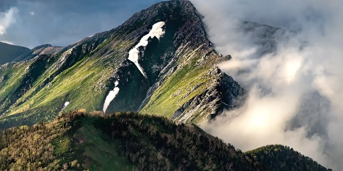 A dramatic mountain ridge with green slopes and wispy clouds, illustrating precision and preparation.