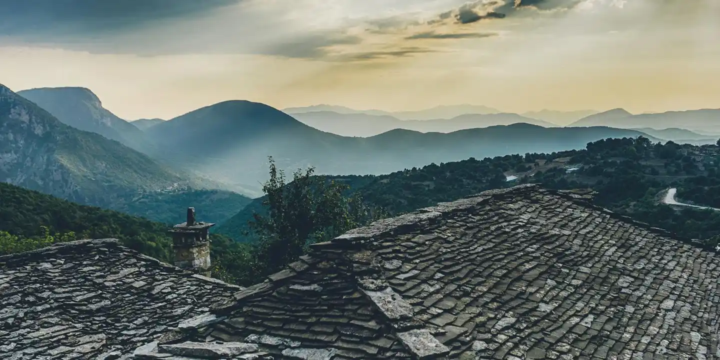 Shingled roof with a stone chimney in the foreground and a misty mountain range in the background.