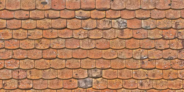 Close-up of weathered clay roof tiles with interlocking edges, showing the area where a new roof would tie into the existing structure.