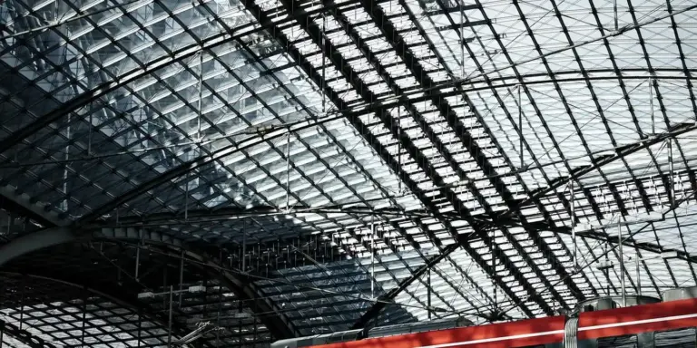 Interior view of a large glass-and-metal roof with a network of trusses and skylight panels, showing complex roof framing.