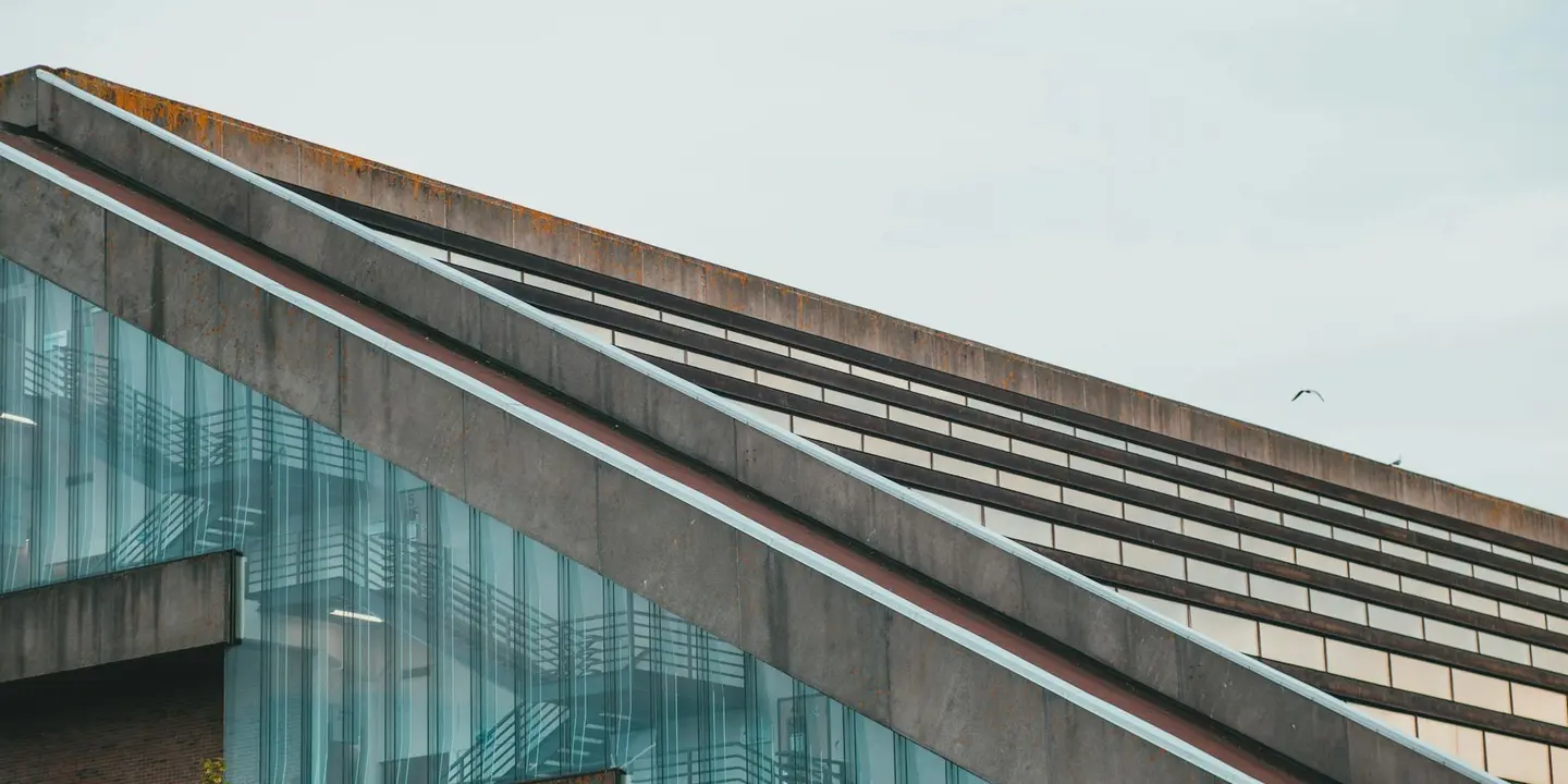 Diagonal sloped metal roof panels on a building with glass siding, illustrating the complexity of roof slope.