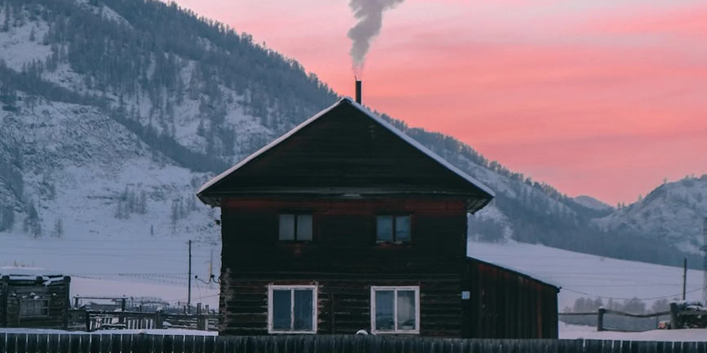 Snow-covered wooden cabin in a wintry landscape with smoke rising from a chimney, illustrating flue safety for pellet stoves and grills.