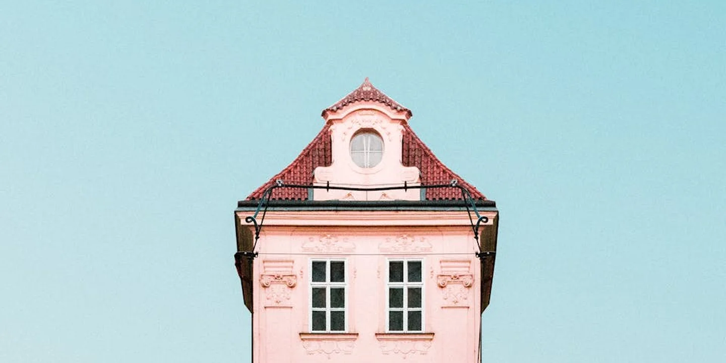 Exterior view of a building with a red-tiled roof and light pink facade against a clear blue sky, showing the roof edge where the tie-in will occur.