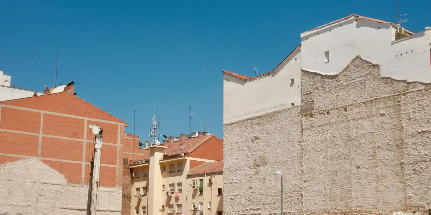 Row of urban rooftops and building facades under a clear blue sky, showing varied roofing materials.