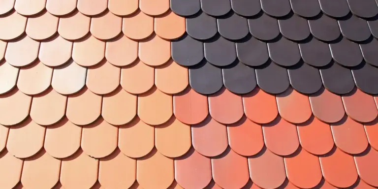 Close-up of overlapping curved clay roof tiles in peach and navy tones, showing the texture and pattern of a tiled roof.