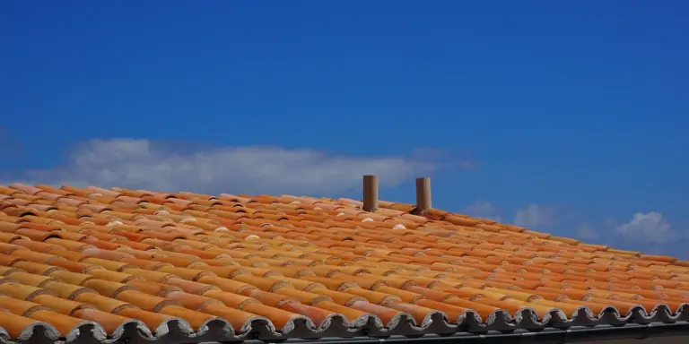 Terracotta tile roof under a bright blue sky with two vent pipes on the ridge.