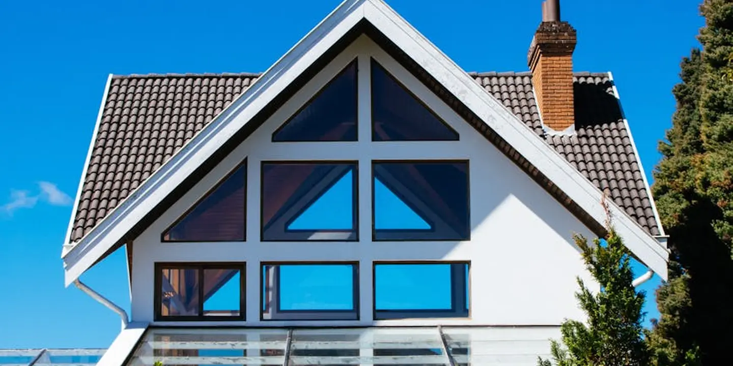 Pitched white house roof with a large front-facing gable and multiple glass windows beneath a clear blue sky.