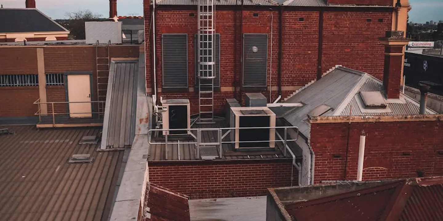 Rooftop deck area on a brick building under construction, featuring a raised platform with metal railing, exposed framing, and a ladder against the wall.