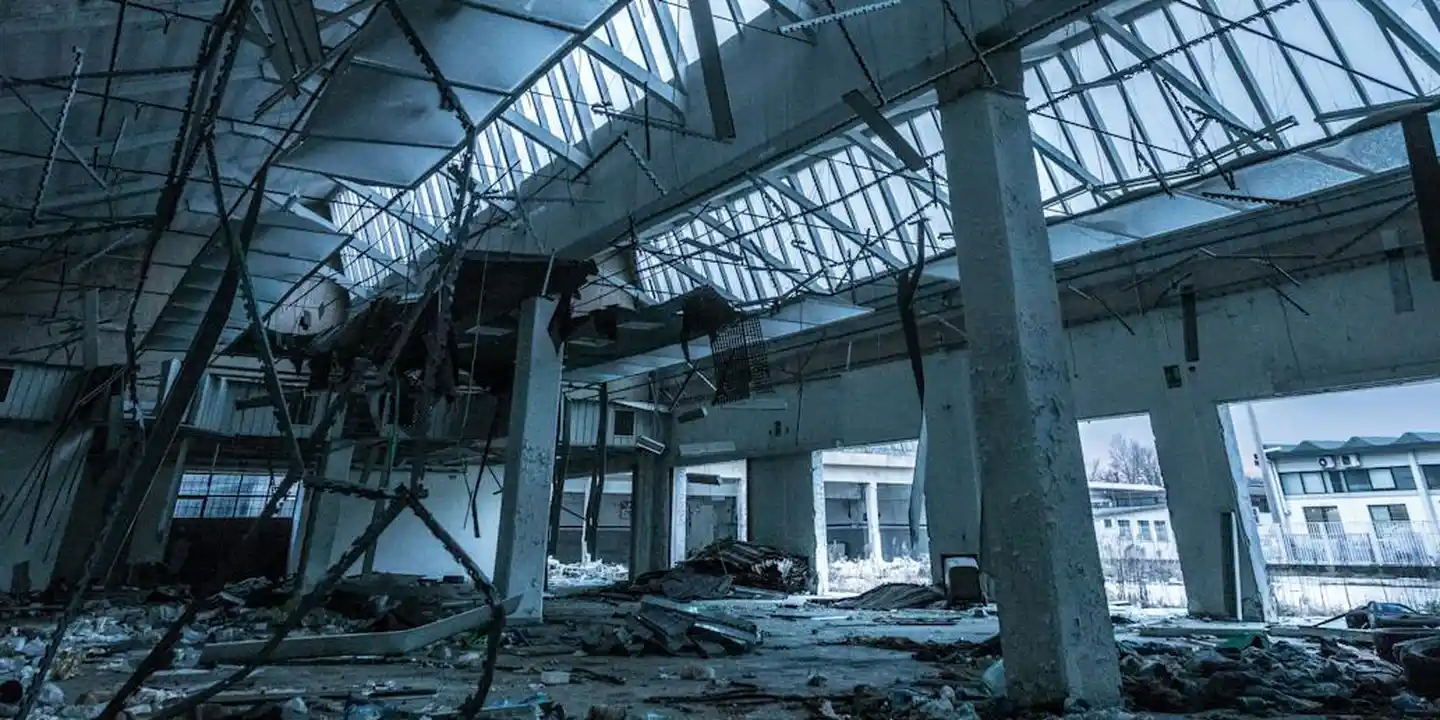 Interior of a damaged building with a collapsed ceiling and scattered debris, showing structural damage from a roof failure.