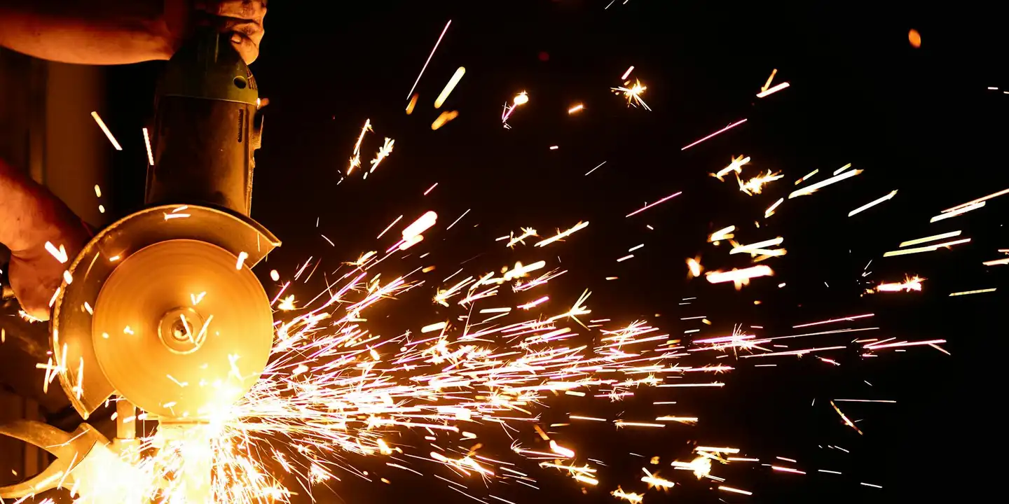 Worker using a power tool with bright sparks flying, cutting metal flashing for roofing