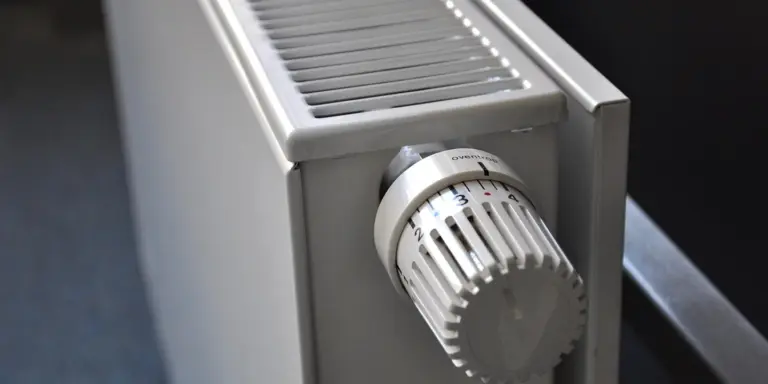 Close-up of a white rotary thermostat dial on a metal baseboard heater.