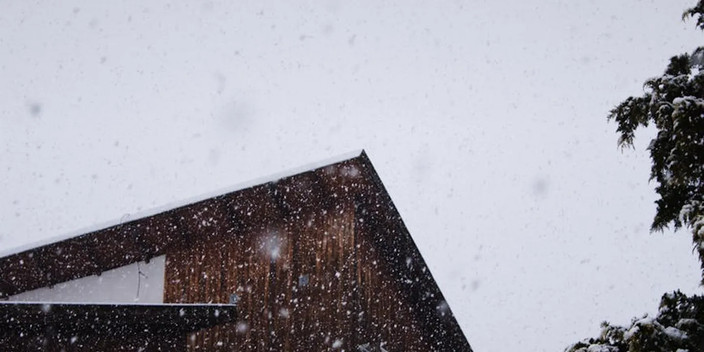 Snowfall over a sloped roof with snow on the surface in a snowy setting