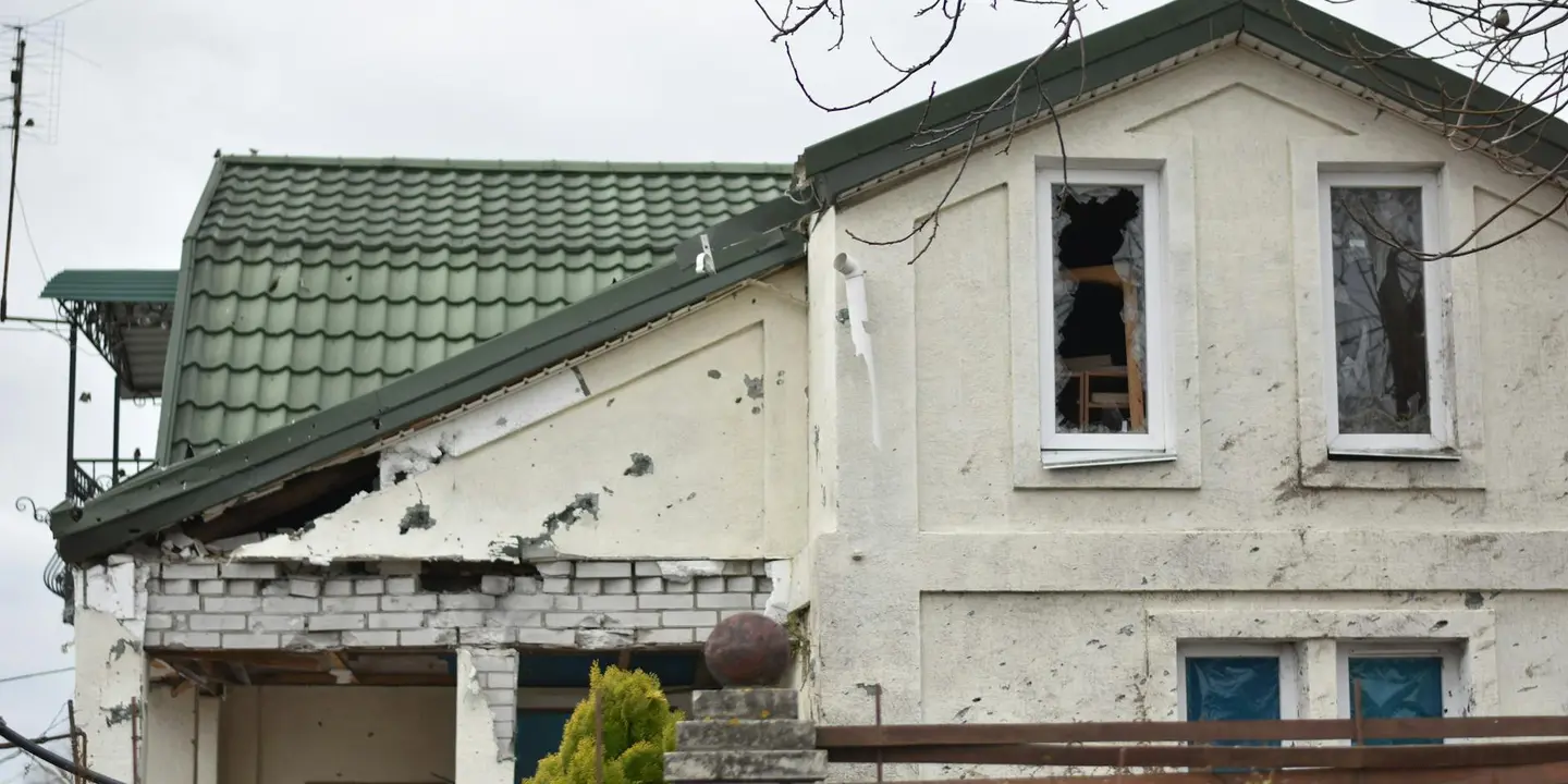 Two-story house with roof damage and cracked exterior wall, including a broken window, illustrating the effects of a roof leak.