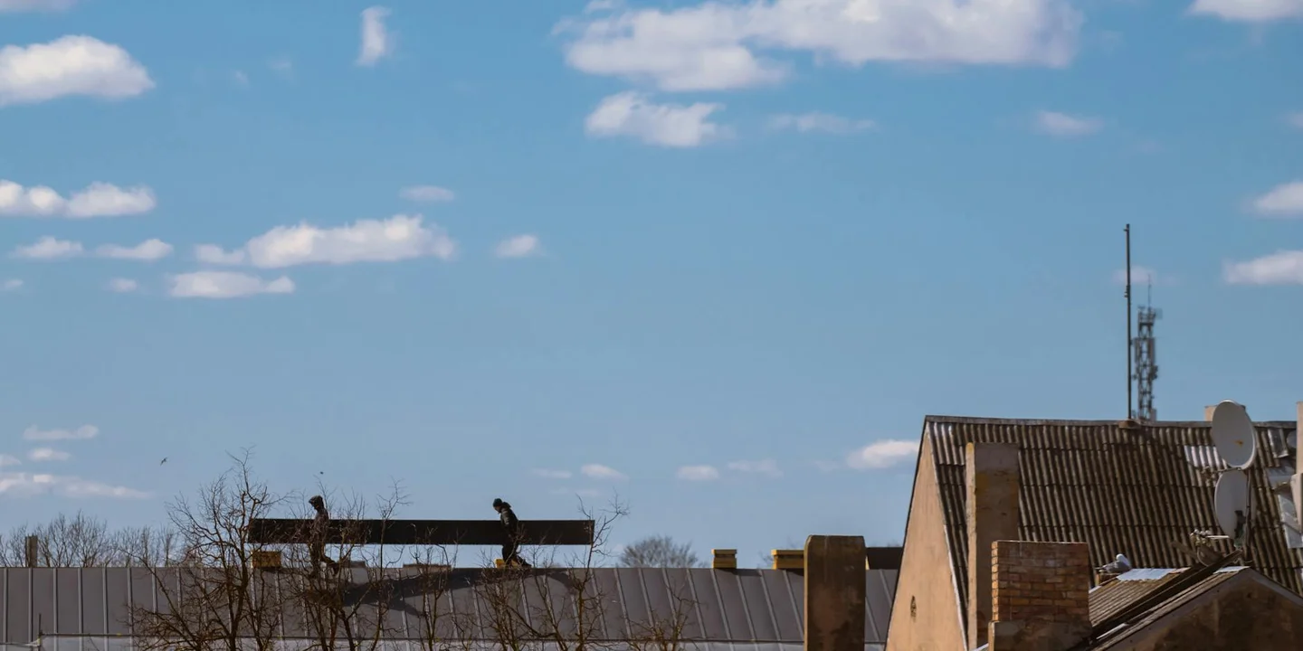 Residential roof with vents and patchwork under a bright blue sky, illustrating the choice between repairing small leaks and replacing the roof.