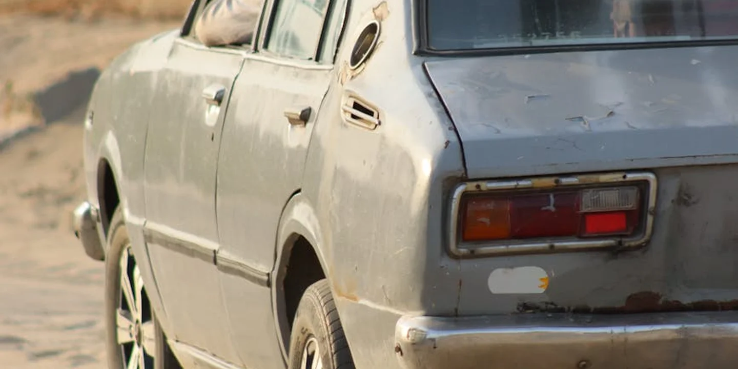 Dusty blue sedan with a roof rack parked on a dirt road.