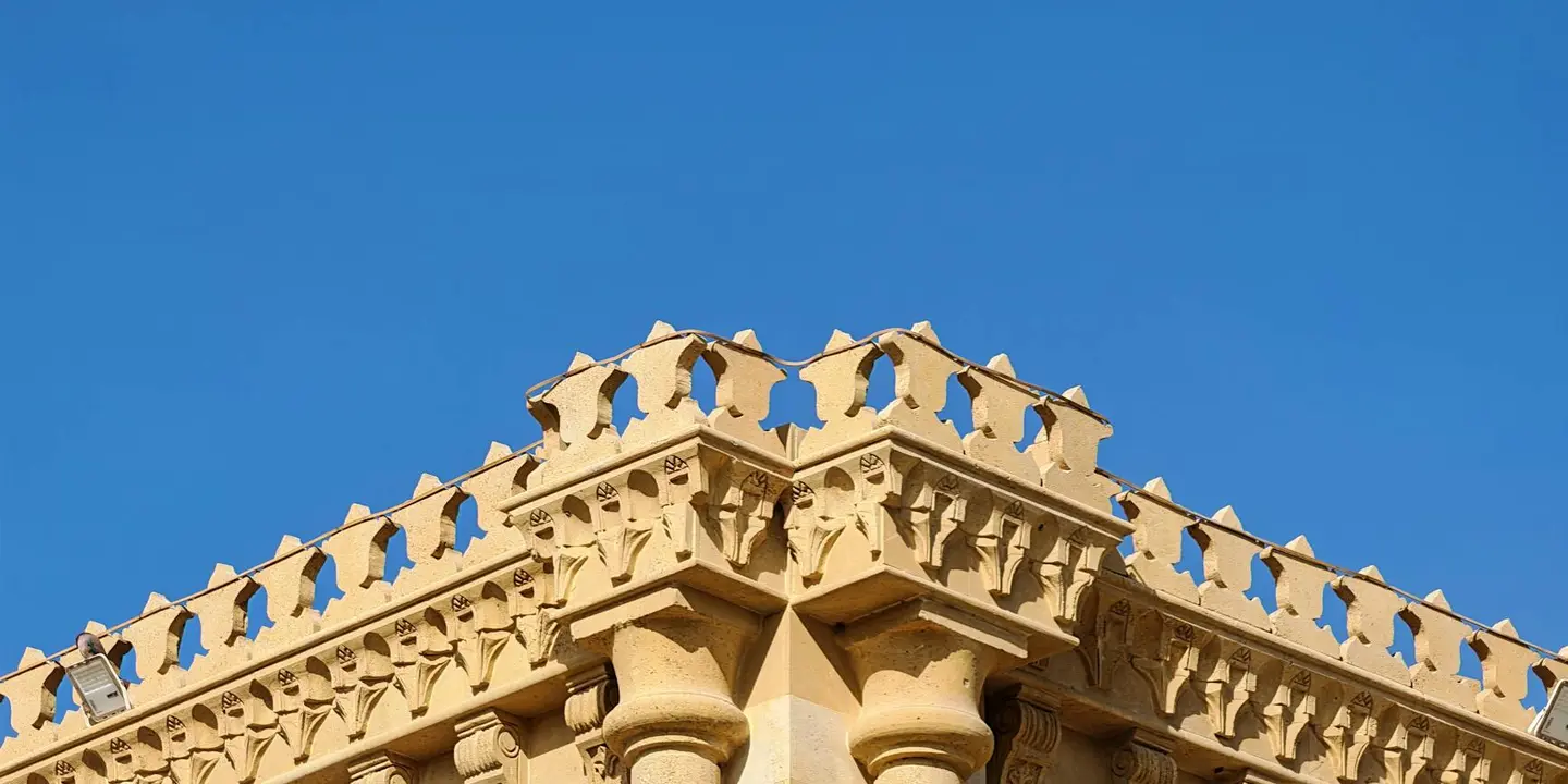 Close-up of decorative roof eave with carved trim and rafter tails against a clear blue sky