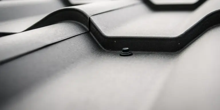 Close-up view of a dark roof tile seam with a small screw head