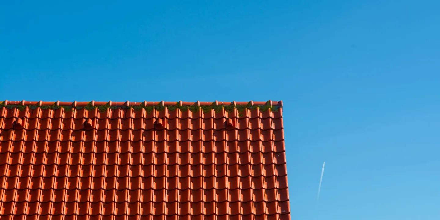 Residential roof with orange clay tiles under a clear blue sky, illustrating roof structure considerations for solar panel installation.