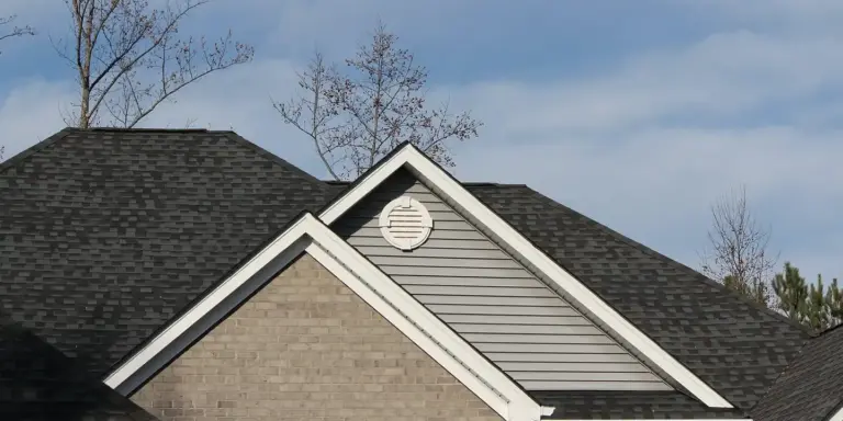 Front view of a residential roof featuring a circular gable vent and visible ridge lines against a blue sky.