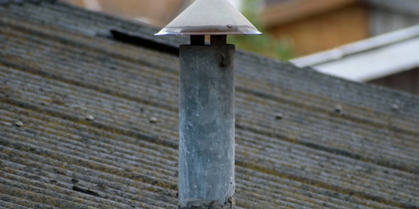 Close-up of a metal roof vent with a cap on a sloped shingled roof