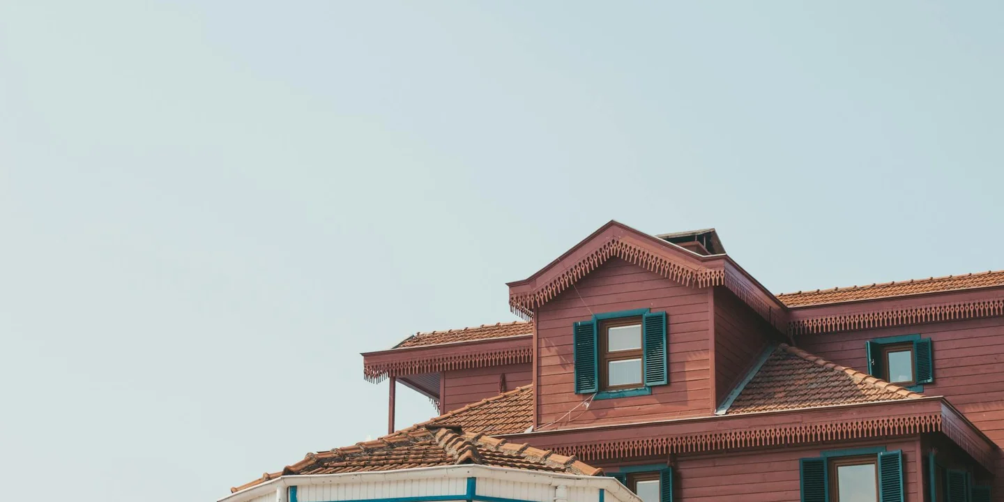 Residential roof with a dormer window and green shutters under a clear sky, illustrating components involved in roof window installation.