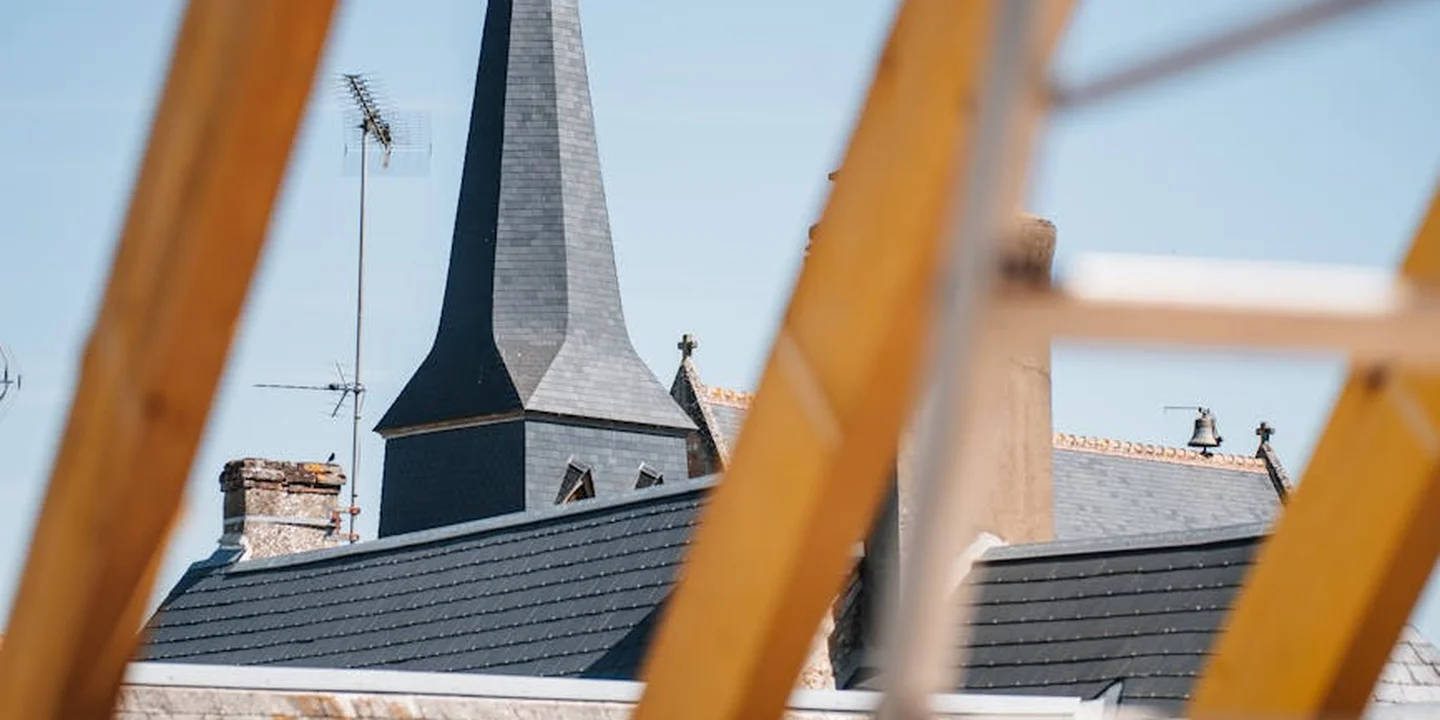Pitched roof framed by wooden scaffolding with a distant church spire, illustrating working at height.