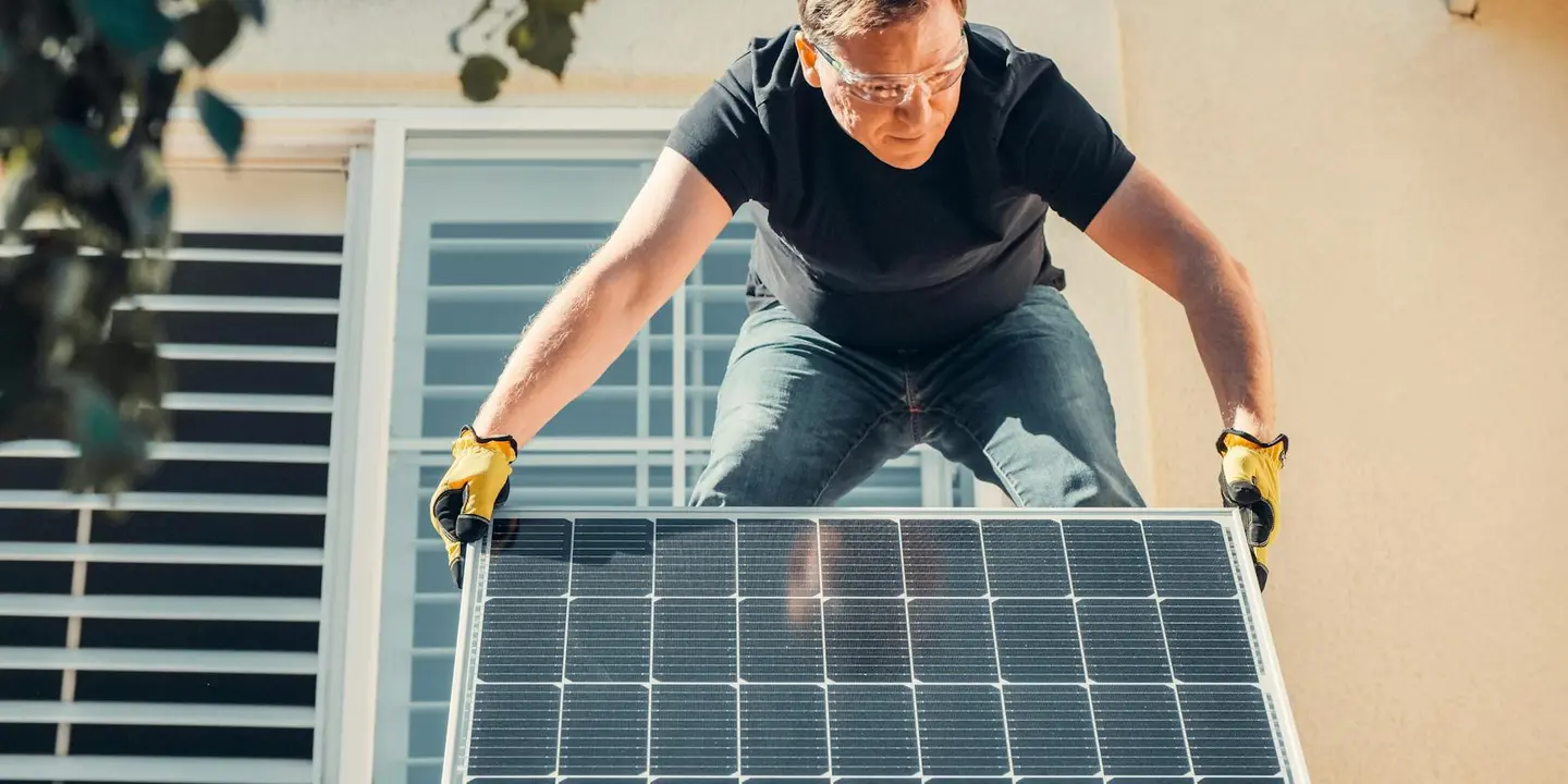 A professional wearing gloves leans over a solar panel mounted on a roof, inspecting for signs of damage and structural issues as part of a roof integrity assessment.