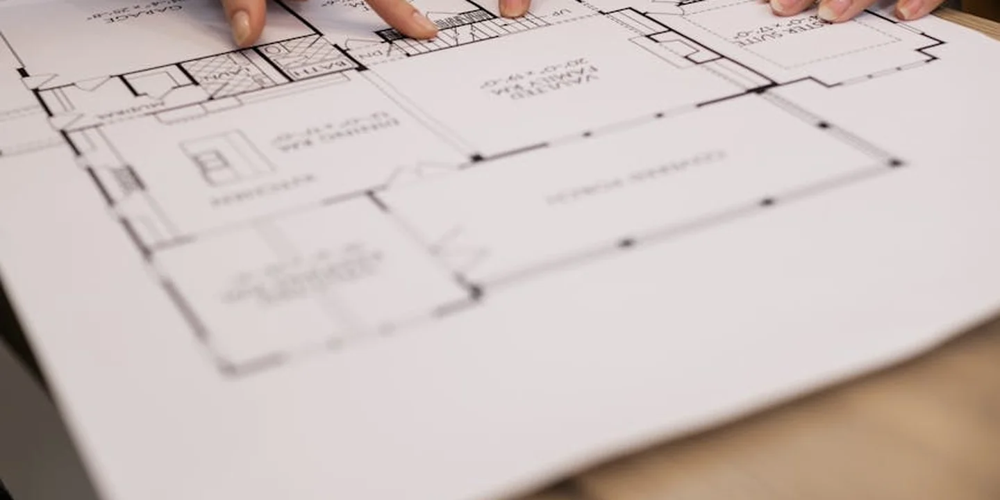 Close-up of hands tracing a roof blueprint with architectural drawings on a desk.