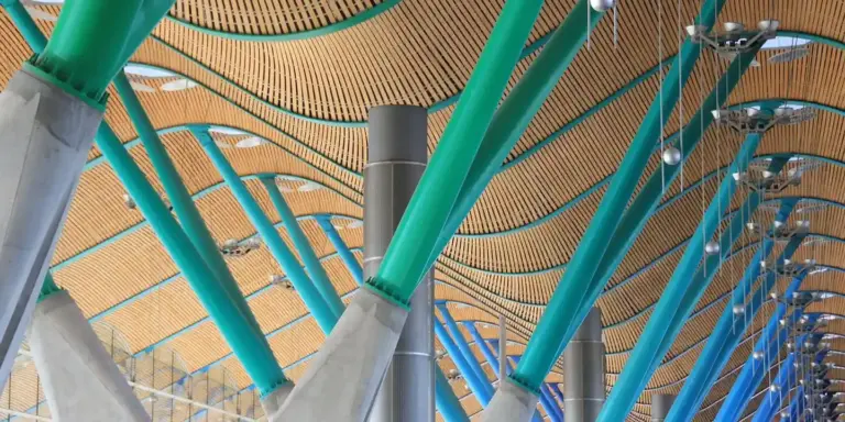 Interior view of a roof structure with teal steel arches supporting a wooden slat roof deck