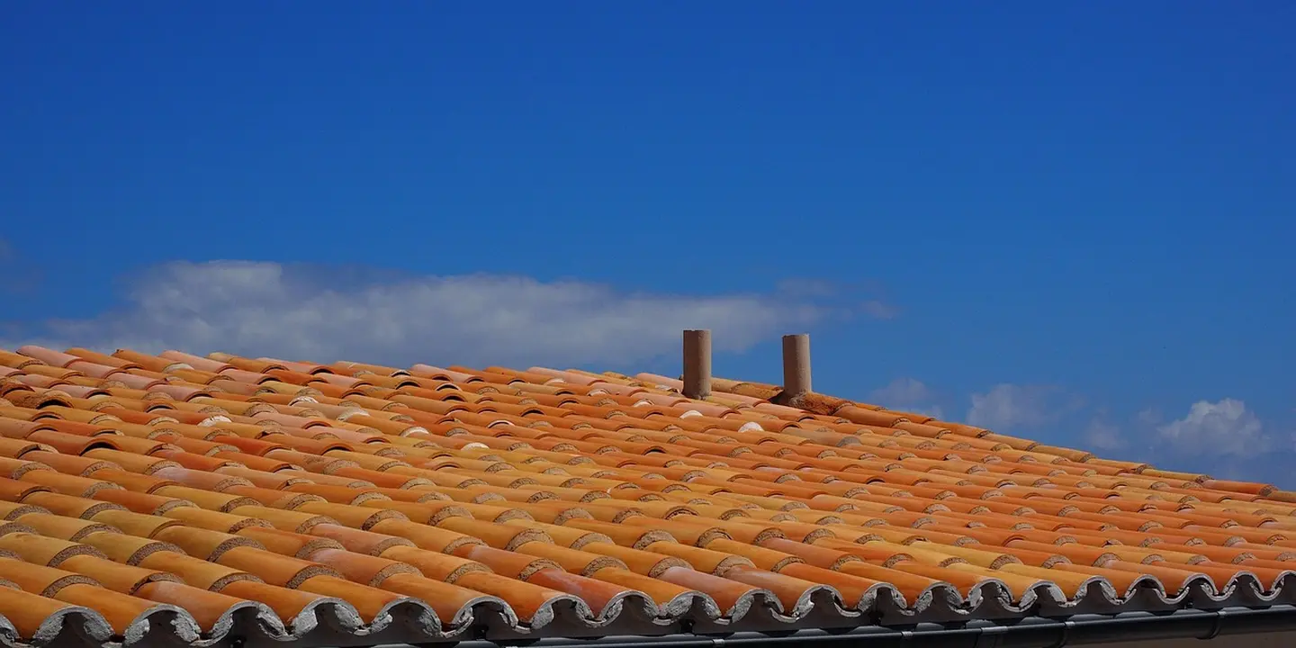 Two vent pipes protruding through a terracotta tiled roof under a clear blue sky.