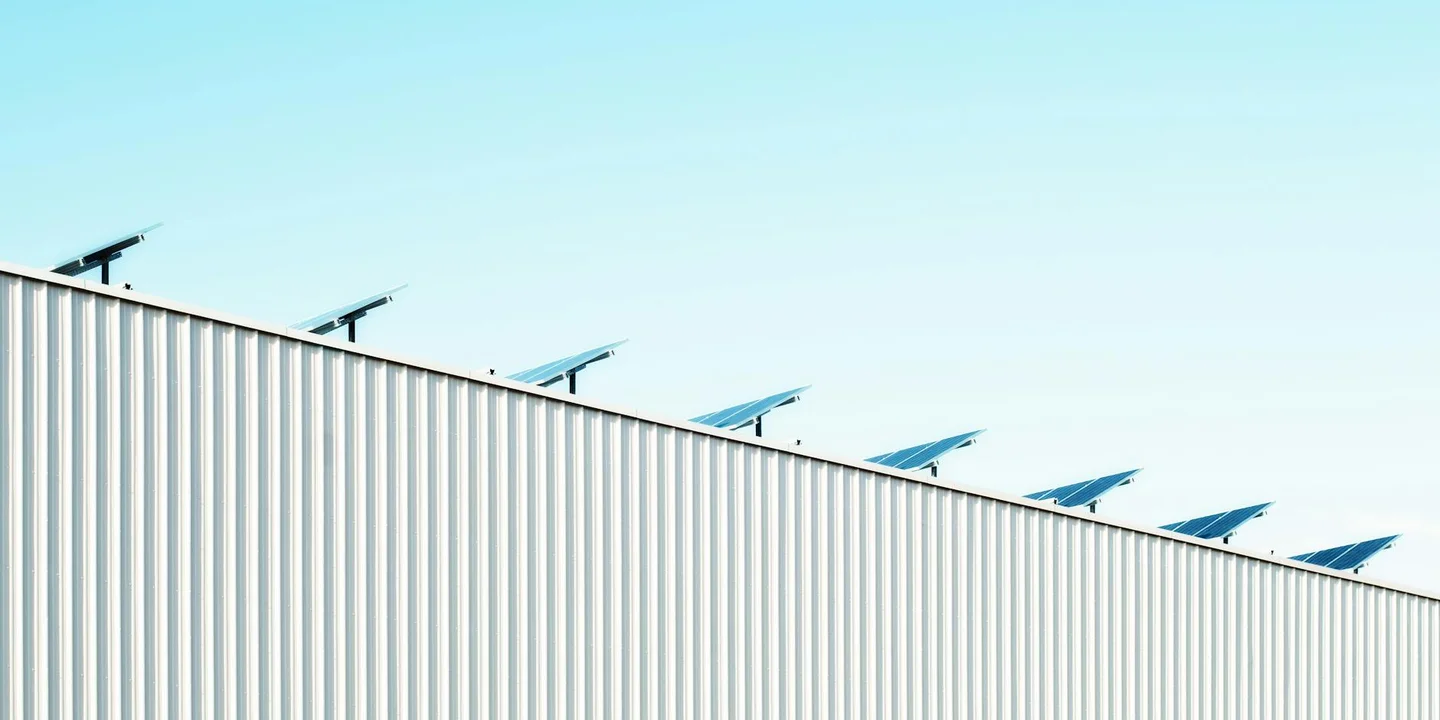 Edge of a metal roof with small solar panels along the ridge under a clear blue sky