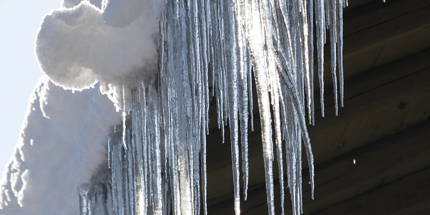 Icicles hanging from a roof edge with snow on the side, illustrating winter gutter challenges.