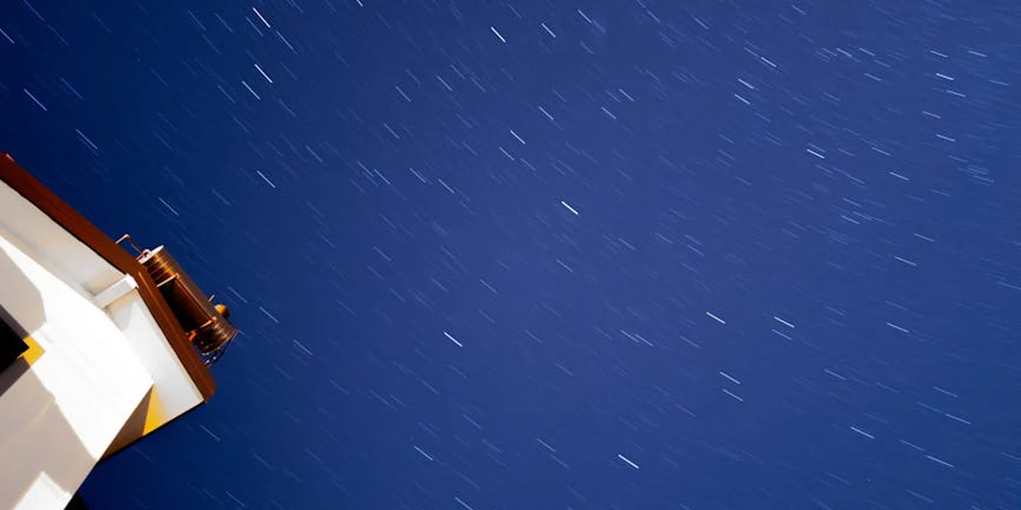 Slanted roof edge of a house at night with a dark blue sky showing star trails.