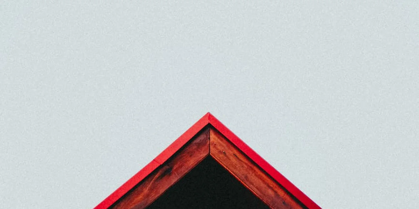 Close-up of a roof ridge with red trim against a gray cloudy sky.