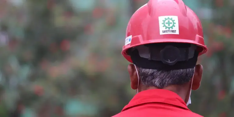 Back view of a construction worker wearing a red hard hat with a Safety First sticker outdoors