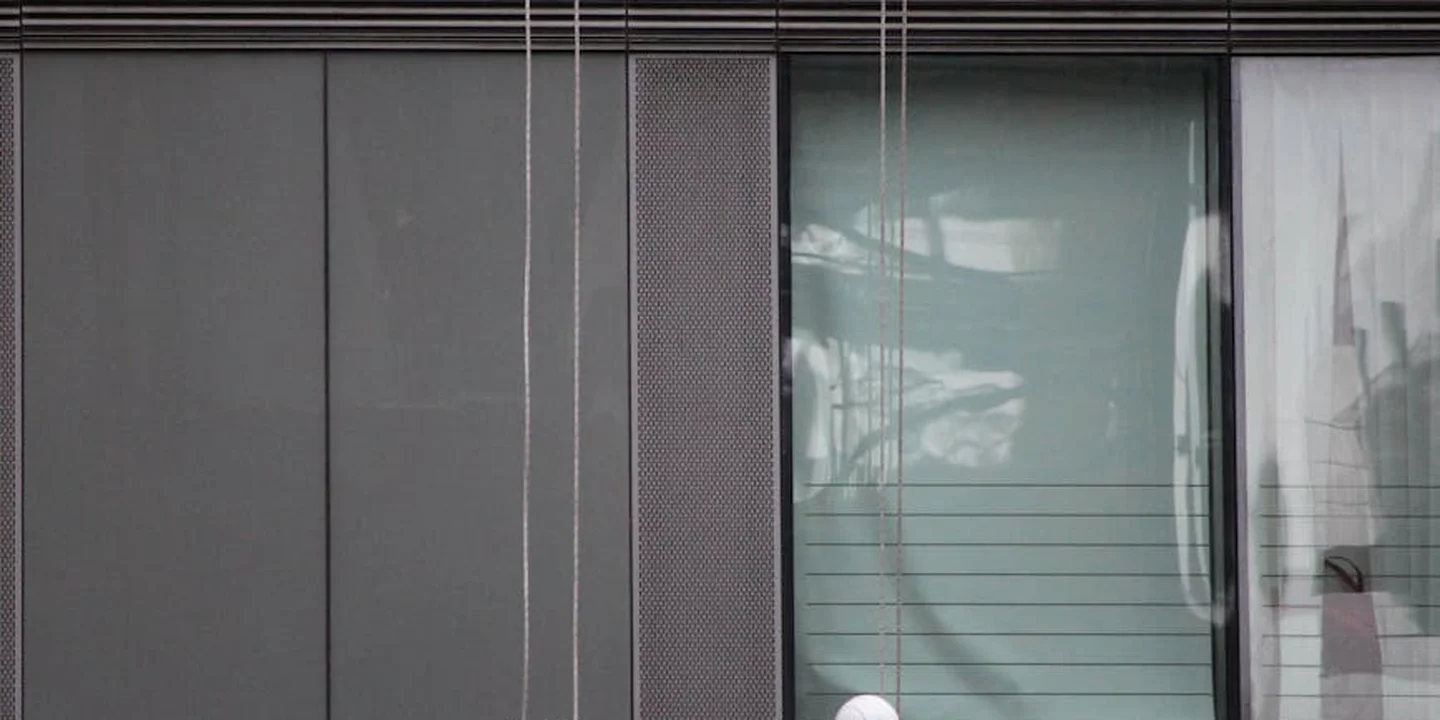 Facade of a building with vertical lines and a window; several ropes or cords hang down, suggesting risky access to a roof.