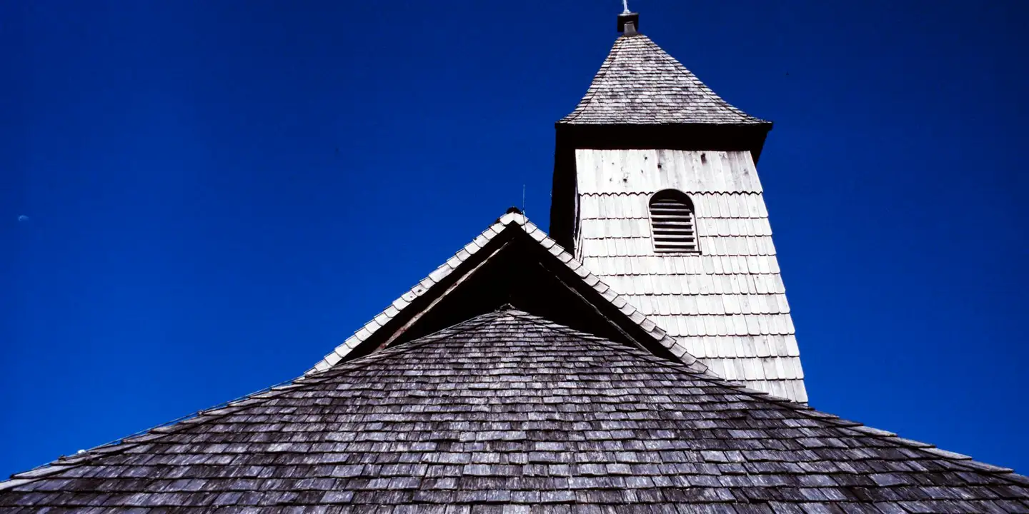 Roof with weathered shingles and a small cupola against a bright blue sky.