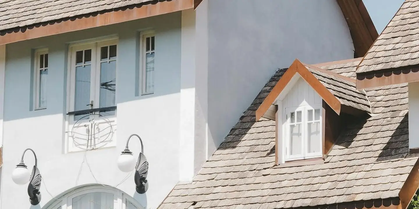 Side view of a house roof with multiple gable dormers covered in brown asphalt shingles.