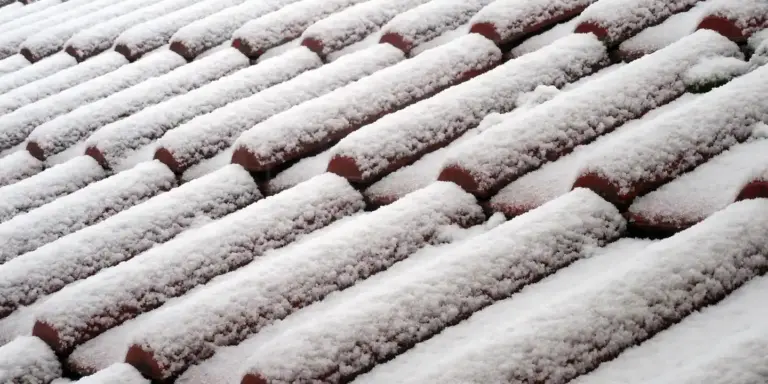Snow-covered clay roof tiles on a sloped roof, illustrating winter weather and wet working conditions