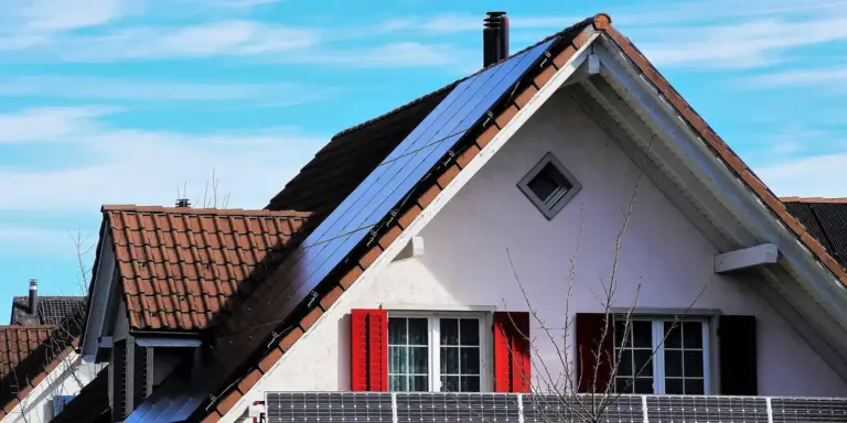 A residential house with solar panels installed on the sloped roof and red window shutters.
