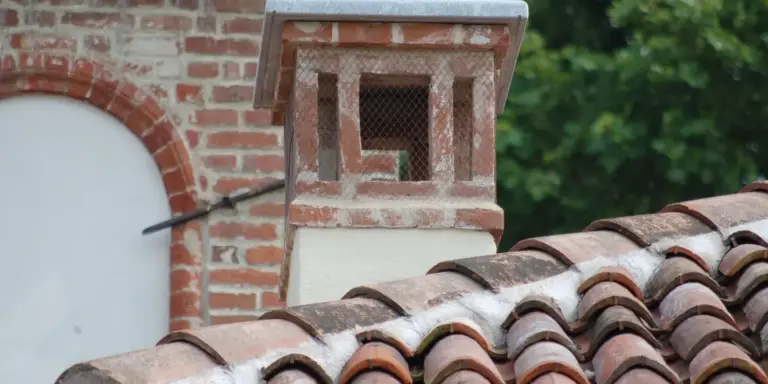 Close-up of clay roof tiles with a brick chimney on a sloped roof.