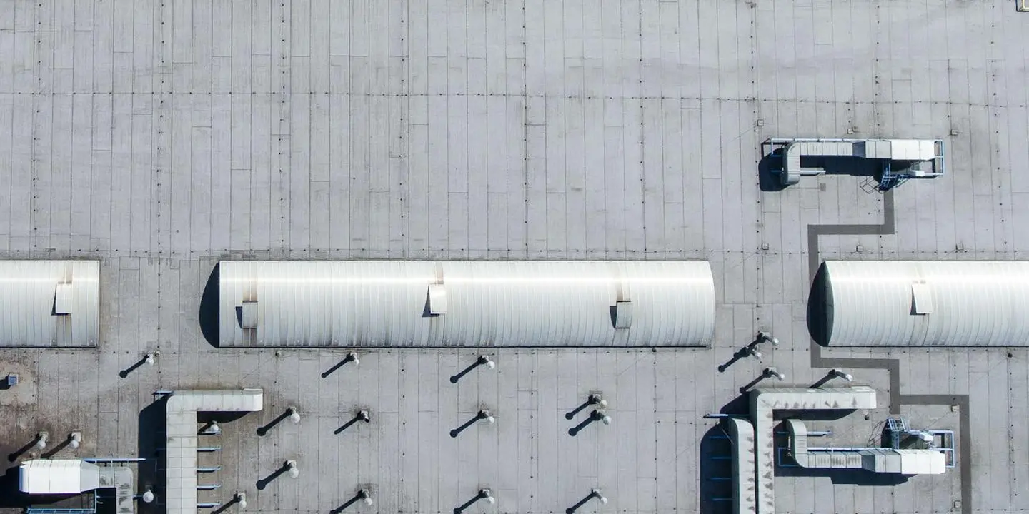 Aerial view of a flat roof featuring multiple metal vent pipes and ventilation ducts to be inspected for damage or blockages.