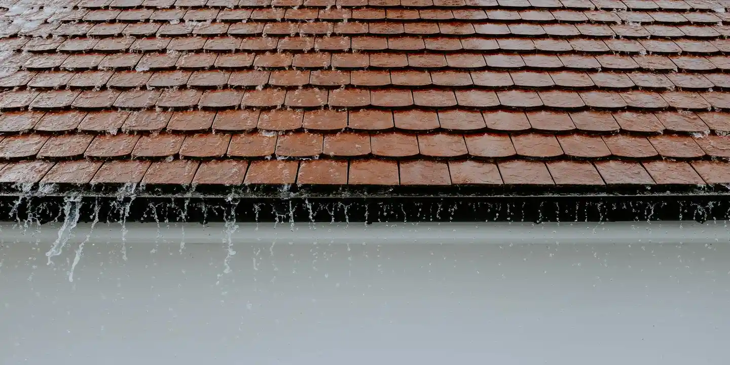 Close-up of a red-tiled roof with a gutter along the edge and water dripping from it.